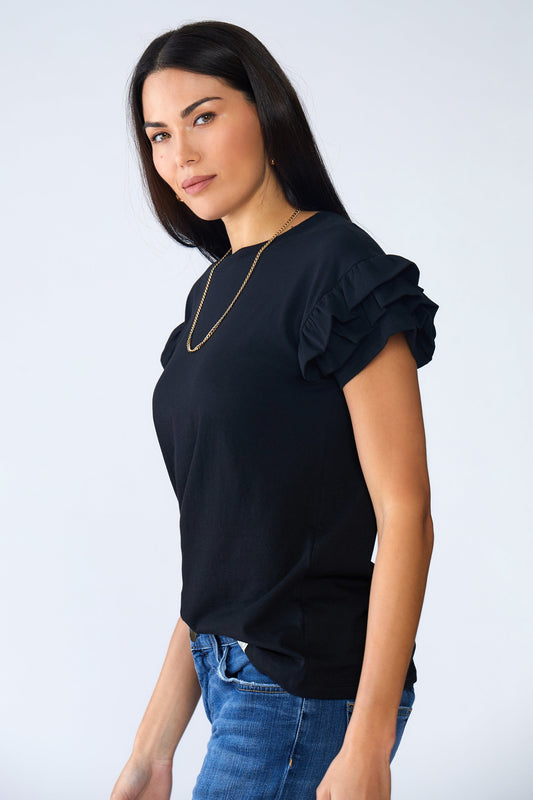 Woman wearing a black top with ruffled sleeves and blue jeans on a light gray background