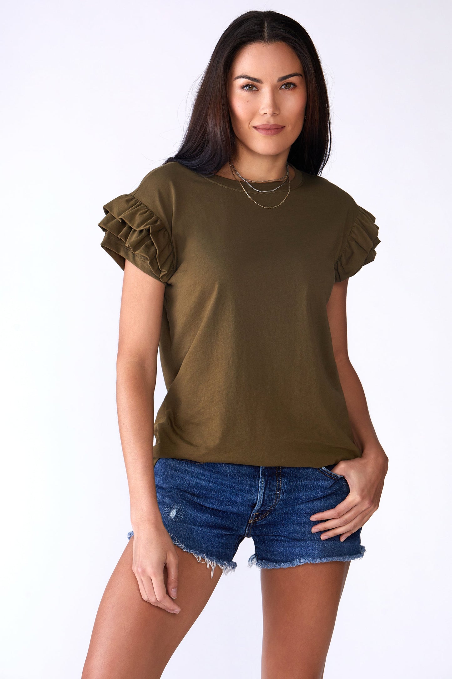 Woman wearing an olive green ruffled sleeve top and denim shorts on a white background